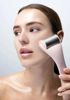 Femme utilisant un rouleau froid pour la peau rose pour apaiser et rafraîchir le visage